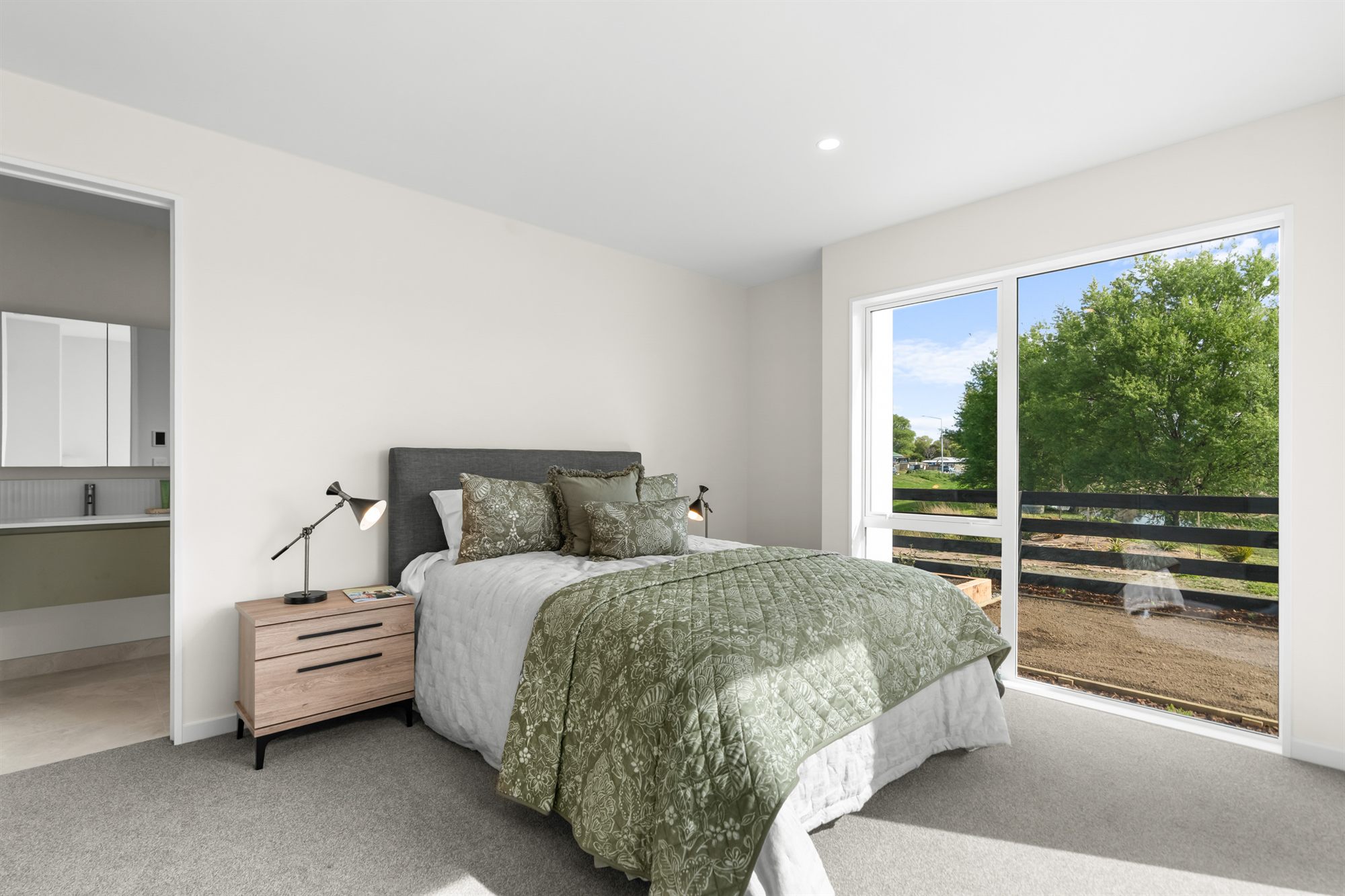 A staged master bedroom at an Elmbridge Mews home — ensuite alongside, garden views through full-height sliders